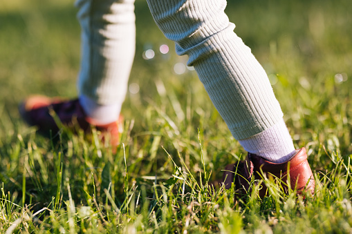 Cropped photo of child's legs walking on grass wearing red shoes.