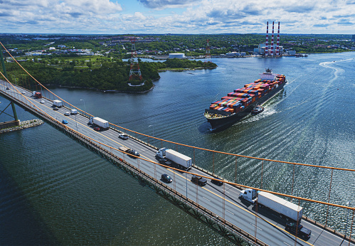Aerial drone view of a container ship about to navigate beneath a suspension bridge.