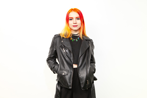Studio portrait of an 18 year old woman with brightly dyed hair in a black leather jacket on a white background