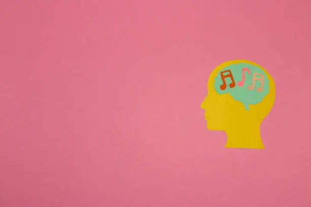 Photo of yellow head with a brain with notes, listening to music, pink background with copy space, creative modern design