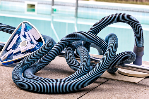 Pool cleaner and tubing is discarded beside the pool after manually used to clean the bottom