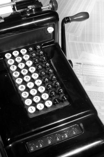 This is an image of a vintage adding machine with ledger paper and a tax return.