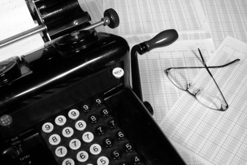 This is an image of an old fashioned adding machine and ledger paper with glasses.