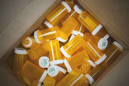 A cardboard box full of empty prescription pill bottles.