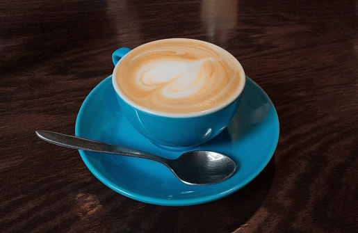 Cream coffee in bright blue cup on wooden table