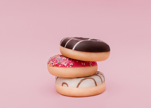 Mixed frosted sprinkled donuts on pink backdrop