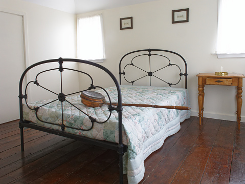 A copper bed warming pan with a long wooden handle lying across a double bed with iron bedstead.