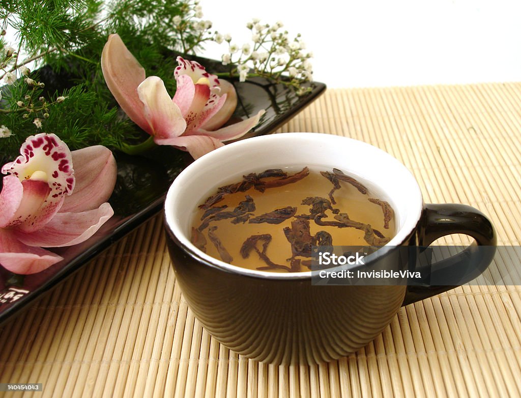 Tasse de thé avec des orchidées sur une assiette de paille matt - Photo de Aliment libre de droits