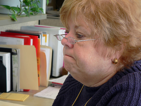 Mature, frowning woman in an office setting.