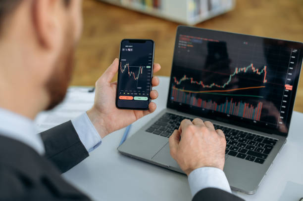 Close-up of a laptop and cellphone screen with stock diagrams. Crypto trader investor broker using cellphone and laptop for cryptocurrency financial market analysis, buying or selling cryptocurrency stock photo