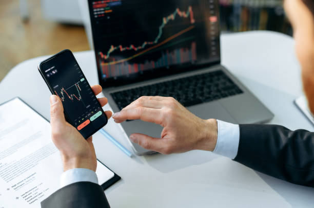 Successful male crypto trader, investor, using a laptop and smartphone, analyzes trading charts in the stock market of a digital cryptocurrency exchange, analyzes, buys and sells cryptocurrencies exitoso comerciante criptográfico masculino, inversor, utilizando una computadora portátil y un teléfono inteligente, analiza los gráficos comerciales en el mercado de valores de un intercambio digital de criptomonedas, analiza, compra y vende criptomo
