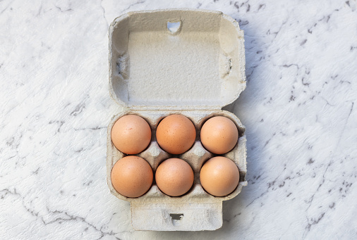 High angle closeup of six eggs in cardboard container on grey textured background (selective focus)