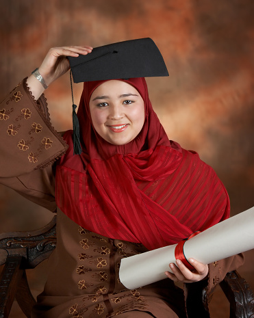 Happy islamic student holding her graduation cap above her traditional veil