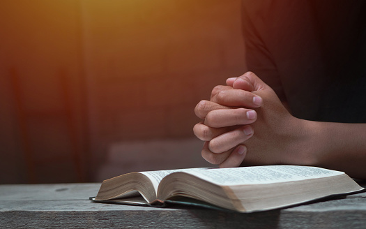 Hands folded in prayer on a Holy Bible in church concept for faith, spirituality and religion, woman praying on holy bible in the morning