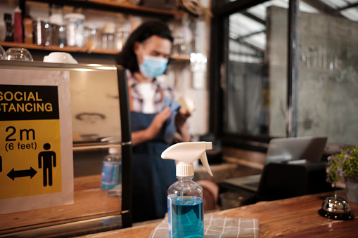 Alcohol sanitizer for healthy protection in a cafe, Asian male barista in face mask use laptop, waiting for coffee order in COVID19 pandemic quarantine, the economic impact for small business startup.