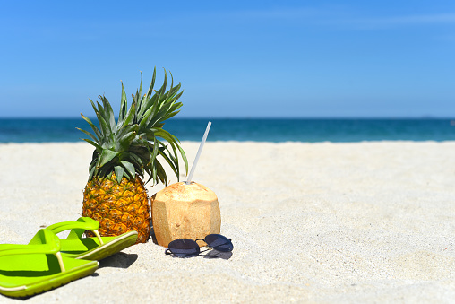 Pineapple with sunglasses, flip-flops and coconut drink on white sand beach in Vietnam