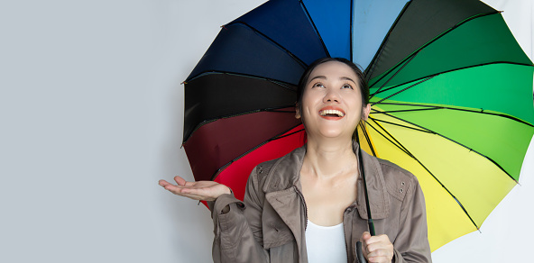 Asian beautiful  woman holding a colorful umbrella looking up to see raining with smile and a happiness