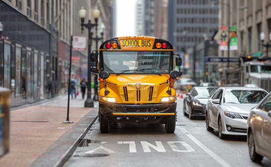 School bus in a USA city center. Yellow classic public bus on the street, only bus lane, American city downtown
