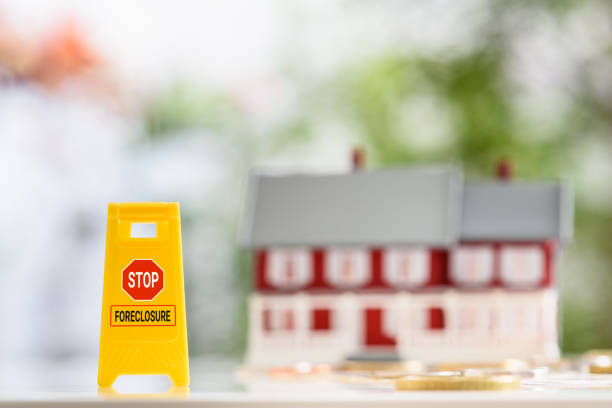 Strategies or ways to stop foreclosure or avoid foreclosure, mortgage relief, financial concept : Yellow sign board with the words STOP FORECLOSURE, a red-white two story house with coins on a table. estrategias o formas de detener la ejecución hipotecaria o evitar la ejecución hipotecaria, el alivio hipotecario, el concepto financiero: letrero amarillo con las palabras stop foreclosure, una casa roja-blanca de dos pisos con monedas sobre una mesa.