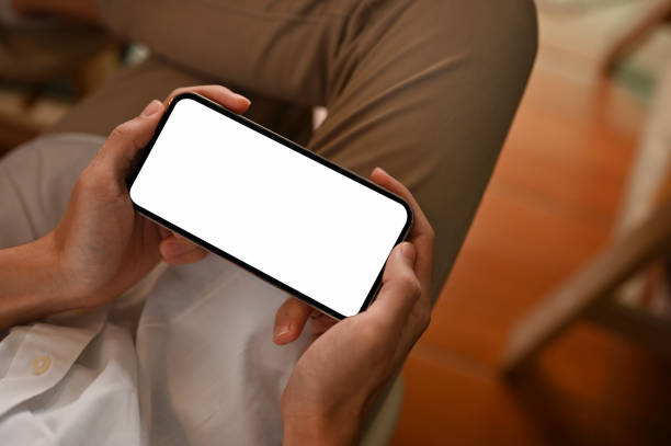 istock Close-up, A young man sitting on the chair, using smartphone. Phone white screen mockup. 1404586736