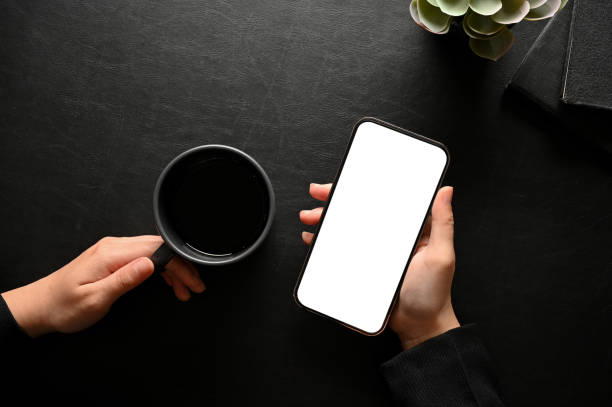 istock A female hand holding a smartphone mockup and a coffee cup over black table background. 1404586807