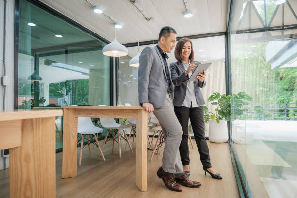 istock Two Asian business people colleagues wearing suit with digital tablet and discussing a project while standing in meeting room at modern office 1404588430