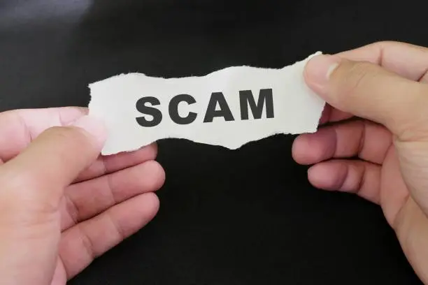 Photo of Scammed victim concept. Hand holding a piece of paper with word scam in dark black background.