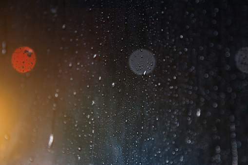 Abstract background with raindrops on window and night blurred light. Rain drops on glass for backgrounds rainy fall autumn weather. Outside window is blurred bokeh water of night city. Copy space