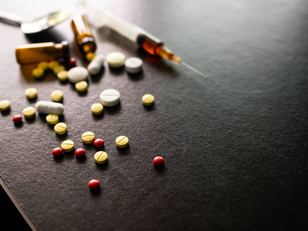 concetto di narcotici. pillole di ecstasy e siringa su sfondo di tavolo di legno nero. - anfetamine foto e immagini stock