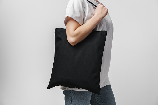 Female holding black cotton bag in her hands on white background, close up