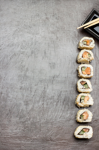 Handful of rice and sushi rolls. Chopsticks and soy sauce in black bowl. Copy space. Flat lay. Dark brown background