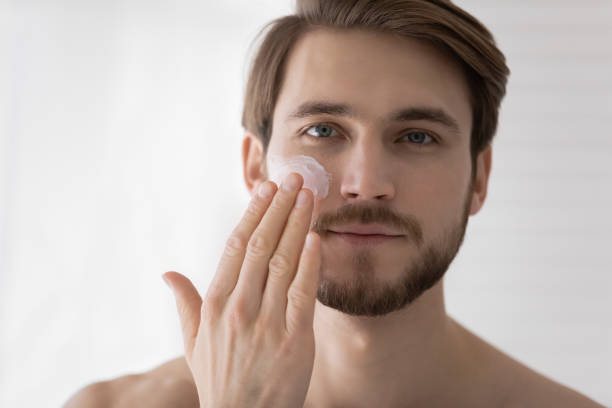 istock Happy young man applying moisturizing cream on cheek. 1404603923