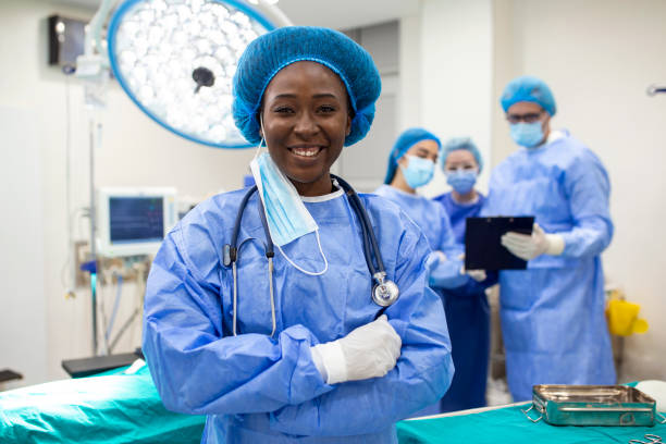 患者に取り組む準備ができて、手術室に立っている幸せなアフリカ系アメリカ人の女性外科医の肖像画。手術劇場で外科用ユニフォームを着た女性医療従事者。 - scrubs surgeon standing uniform ストックフォトと画像