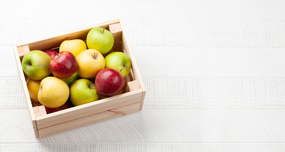 Colorful ripe apple fruits in box on wooden table. Top view with copy space