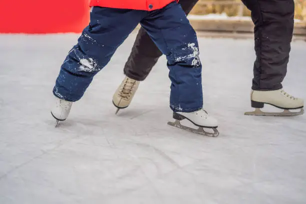 young mother teaching her little son ice skating at outdoor skating rink. Family enjoy winter on ice-rink outdoors.