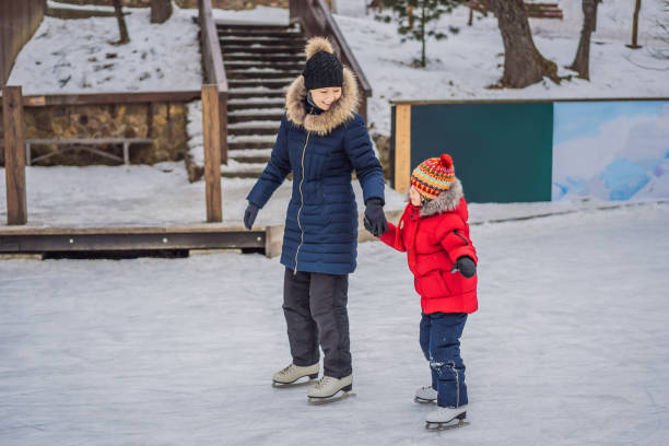 młoda mama uczy swojego małego syna jazdy na łyżwach na odkrytym lodowisku. rodzina cieszy się zimą na lodowisku na świeżym powietrzu - ice skating ice hockey child family zdjęcia i obrazy z banku zdjęć