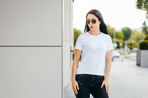 Stylish brunette asian girl wearing white t-shirt and sunglasses posing against street , urban clothing style. Street photography
