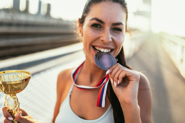 Young female athlete holding her medal. Shot of a young female athlete holding cup while biting her medal. medallist stock pictures, royalty-free photos & images