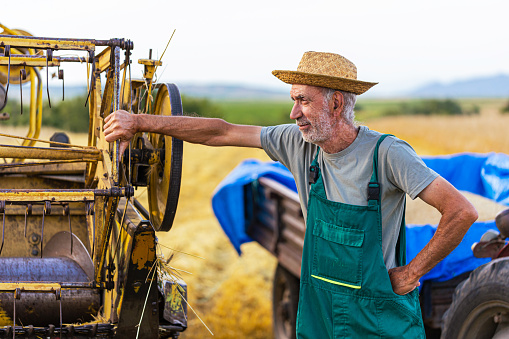 Senior male farmer standing lean on combine harvester