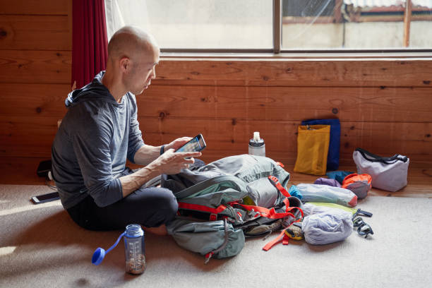 istock Asian man using smartphone to check tomorrow's weather and climbing route while packing luggage at a mountain lodge. 1404614182