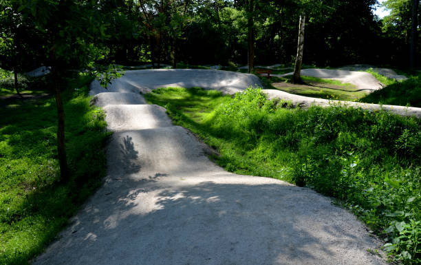 forêt dans laquelle il y a une piste pour les pistes cyclables inclinées virages l’un après l’autre creusé dans le sol dans des formes parfaites vtt même pour les enfants, clairière, soleil, ombres, course neuve, pelouse - bmx flatland photos et images de collection