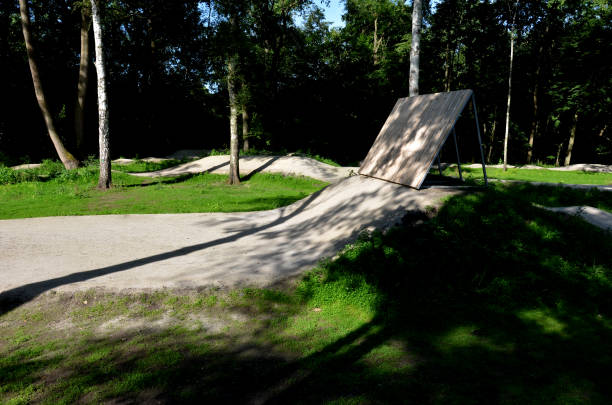 forêt dans laquelle il y a une piste pour les pistes cyclables inclinées virages l’un après l’autre creusé dans le sol dans des formes parfaites vtt même pour les enfants, clairière, soleil, ombres, course neuve, pelouse - bmx flatland photos et images de collection