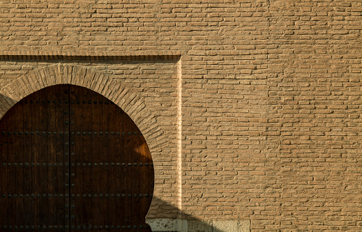 Arch wooden door on brick wall with sunlight and shadow. Granada, Spain