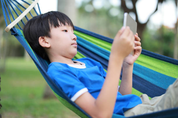 屋外でタブレットを使用する小さな男の子 - swing child swinging front or back yard ストックフォトと画像