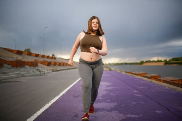 european teenage girl overweight on jog on treadmill along embankment of city, overweight and active lifestyle of teenager - teen obesity imagens e fotografias de stock