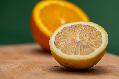 Close up shot of a sliced lemon and orange on a cutting board on a dark green background.