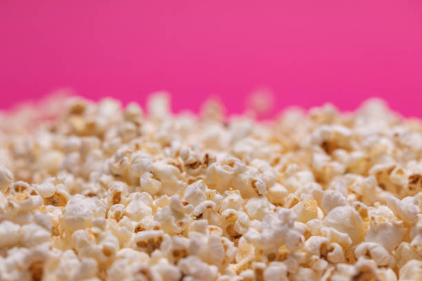 A close-up of a hand holding a handful of popcorn above a glas jar filled with popcorn.