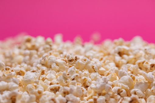 Extreme close up shot of popcorn on a bright pink background.