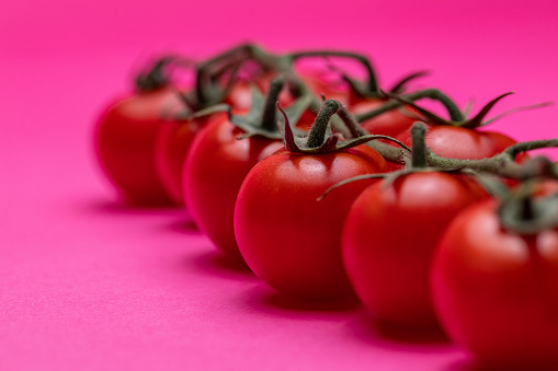 A close up shot of a group of cherry tomatoes on a pink background.