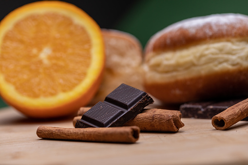 A close up shot of a sliced orange, dark chocolate, shavings of cinnamon and a doughnut on a dark green background.